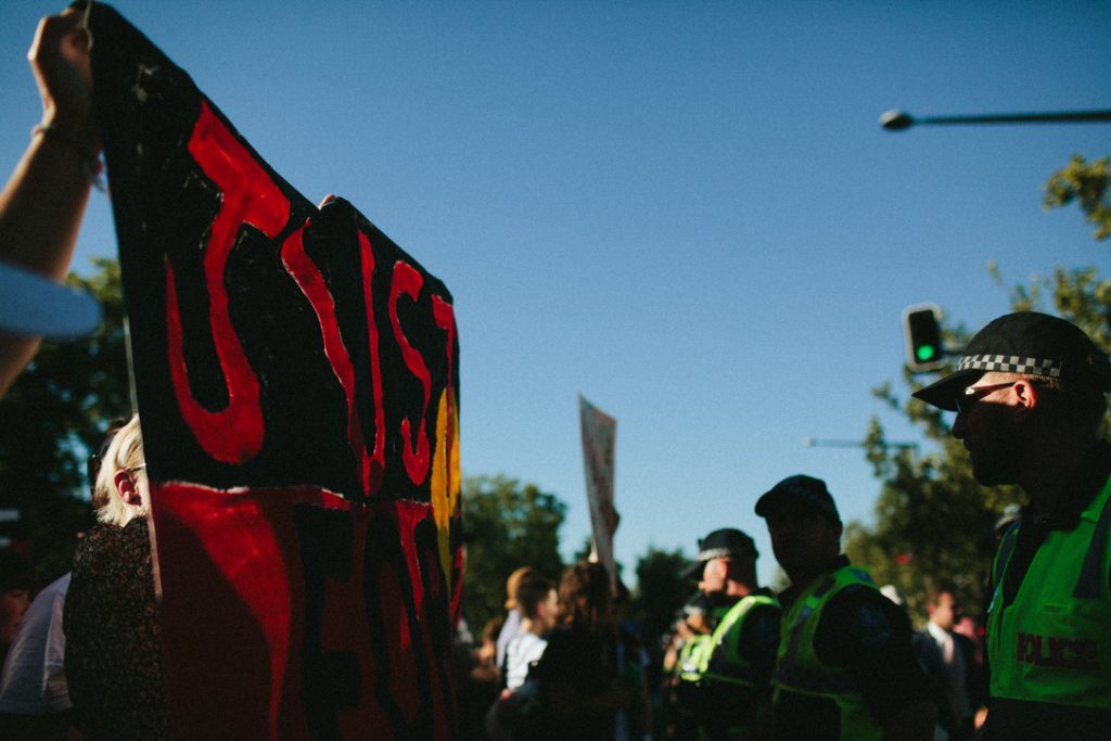 A line of supporters hold ‘Justice for Fella’ banner to a police line at Invasion Day rally.